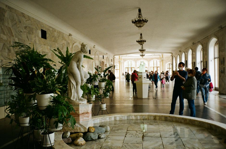 Interior of spacious hall of gallery with classic fountain and marble statue near potted plants against big windows